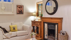 Un salon chaleureux avec une cheminée, un canapé agrémenté d’un coussin jaune, un meuble en bois et un miroir au mur.