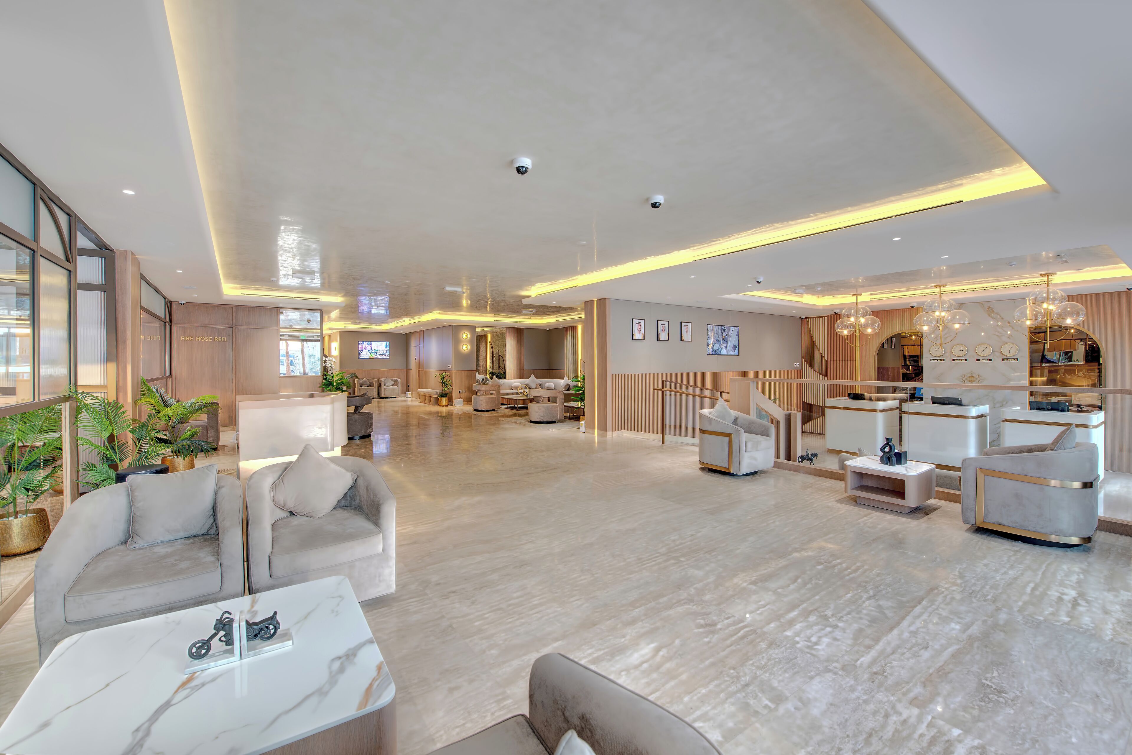 A spacious lobby with a modern design, featuring a seating area with sofas and a coffee table, a reception desk, and a staircase leading to upper floors.