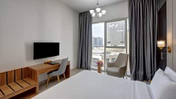 Habitación de hotel moderna con una cama grande, un escritorio con silla, televisión y vistas de la ciudad a través de amplias ventanas.