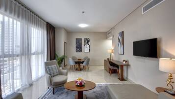 Ein modernes Wohnzimmer mit einer Couch, Sesseln, einem Couchtisch mit Blumen, einem Essbereich mit Stühlen, einem Fernseher und Kunstwerken an den Wänden.
