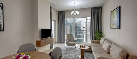 A modern living room with a sofa, a dining table with chairs, a TV, and a large window with a city view.