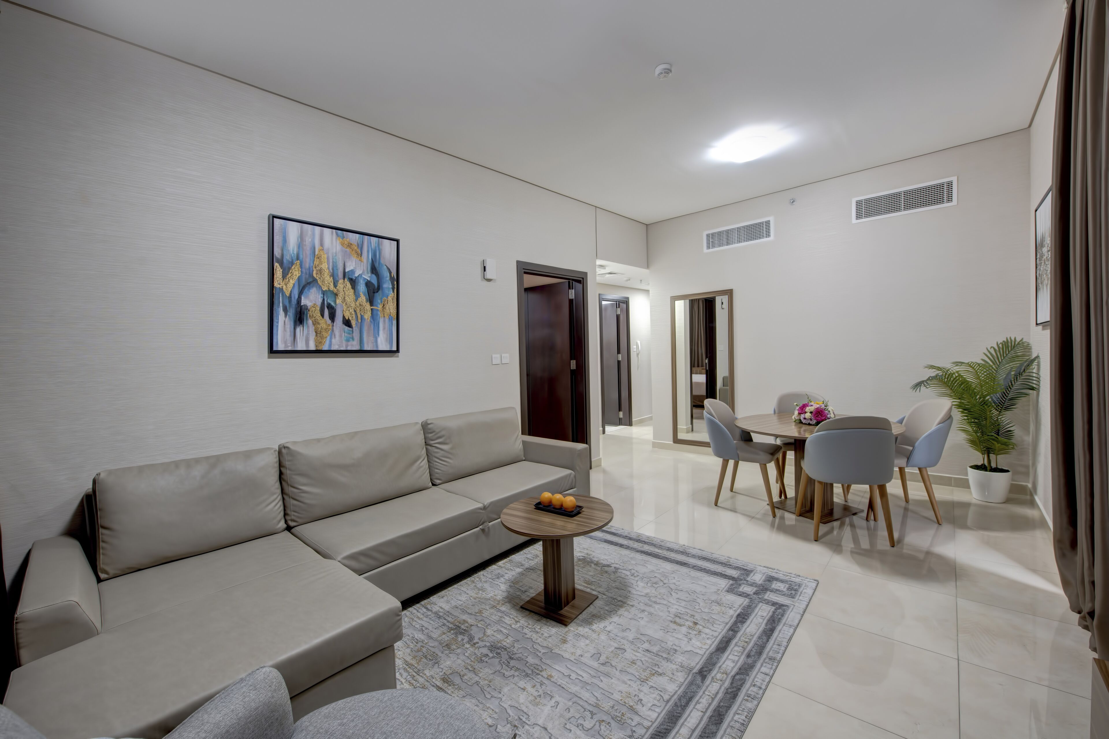 A modern living room with a beige sofa, a round coffee table, and a dining area with a table and chairs.