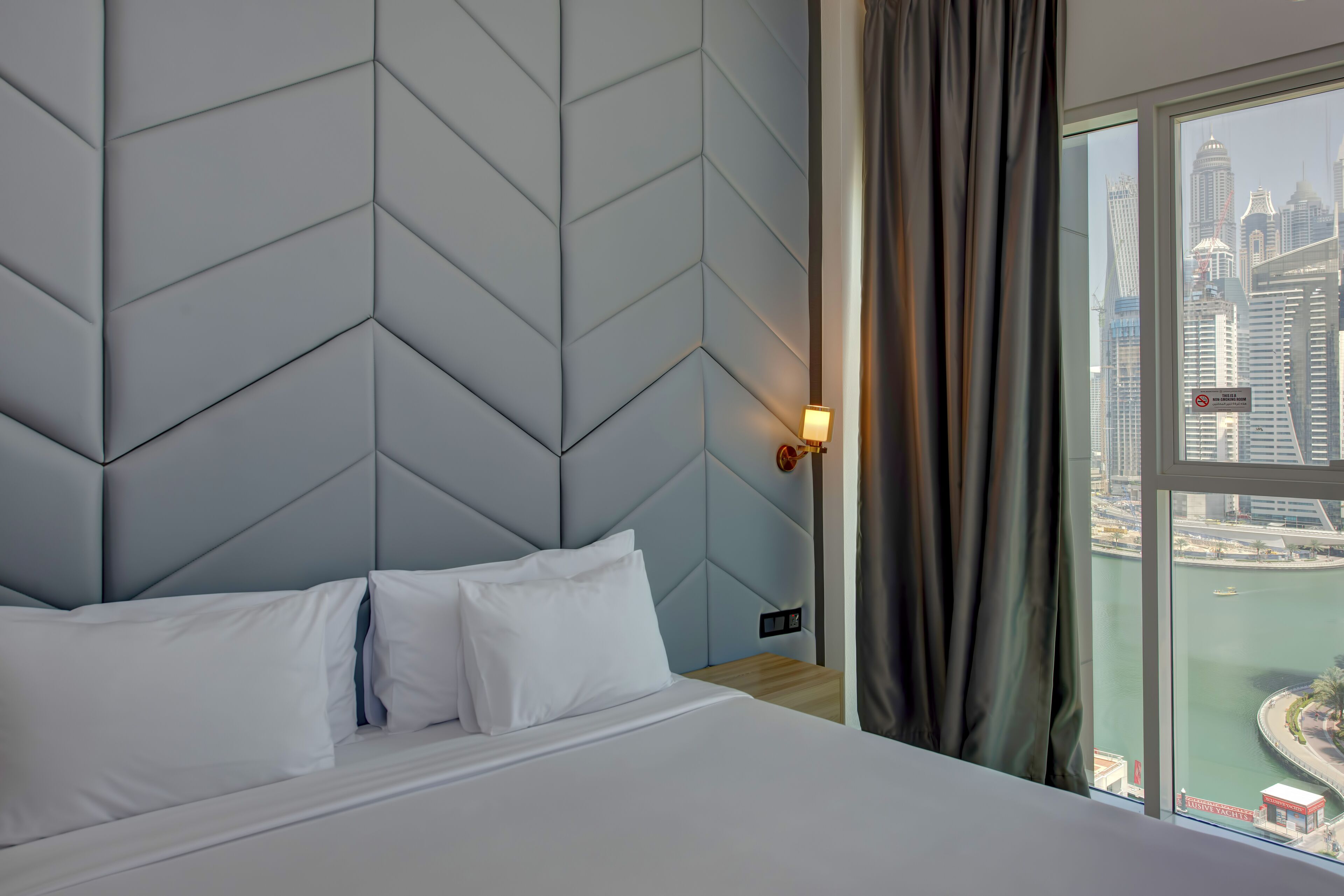 Habitación de hotel con una cama grande, vistas a la ciudad y un cabecero moderno de diseño geométrico.