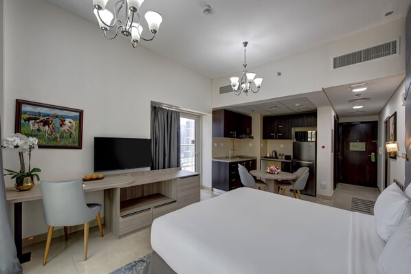 Una habitación de hotel moderna con una cama grande, un escritorio con televisión de pantalla plana, un comedor y una kitchenette.