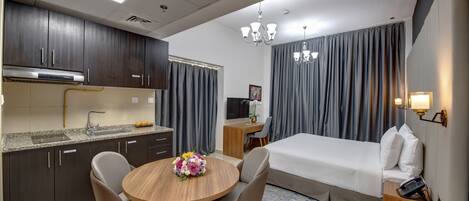 Una habitación de hotel moderna con kitchenette, cama, escritorio y zona de comedor.