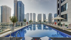 Ein Pool auf dem Dach mit Liegestühlen und Sonnenschirmen, umgeben von Hochhäusern.