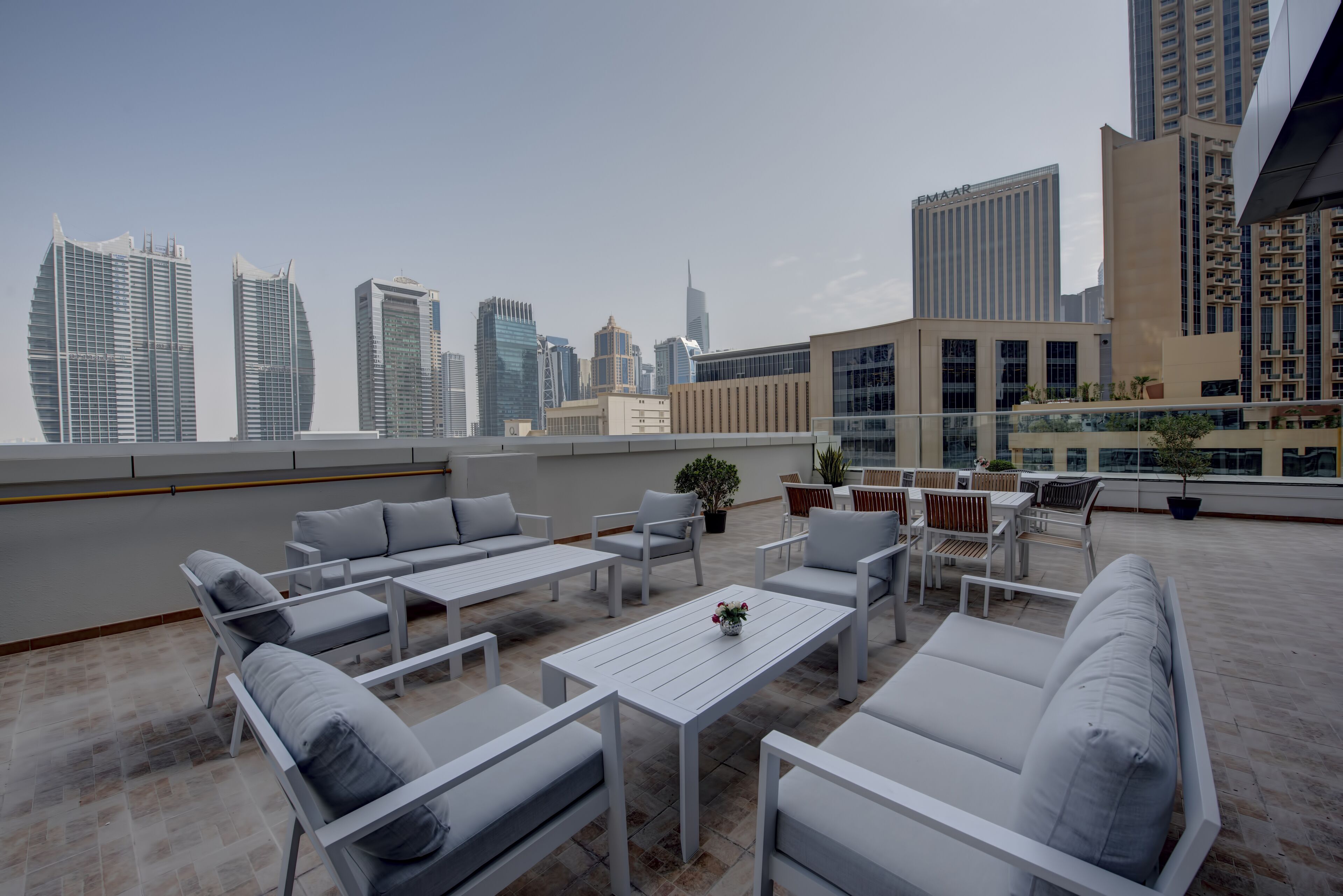 A rooftop terrace with white furniture, a potted plant, and a view of the city skyline.