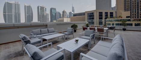 Una terraza en la azotea con mobiliario blanco, una planta en maceta y vistas del horizonte urbano.