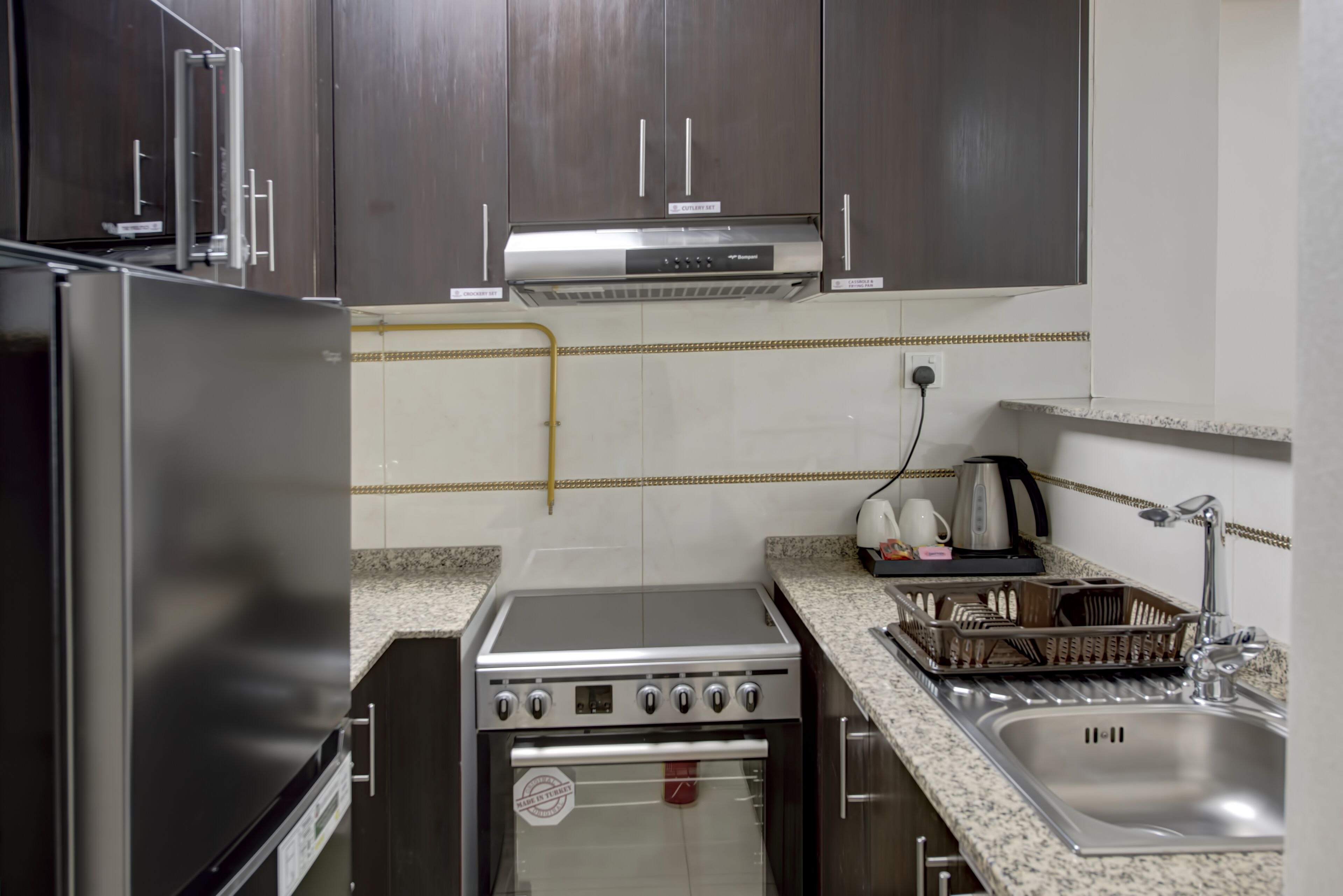 Uma cozinha compacta com armários de madeira escura, fogão de aço inoxidável e forno embutido.