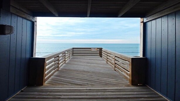 A wooden pier leading to a body of water, enclosed by blue walls. - Steps to the Beach! Just “Wait-N-Sea” what this condo has to offer! (North Topsail Beach)