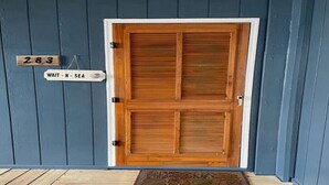 A wooden double door with a white frame, a wooden number plaque '283', and a sign 'WAIT - N - SEA' on the wall. - Steps to the Beach! Just “Wait-N-Sea” what this condo has to offer! (North Topsail Beach)