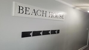A hallway with a sign reading "BEACH HOUSE" and a coat rack with hooks. - Steps to the Beach! Just “Wait-N-Sea” what this condo has to offer! (North Topsail Beach)