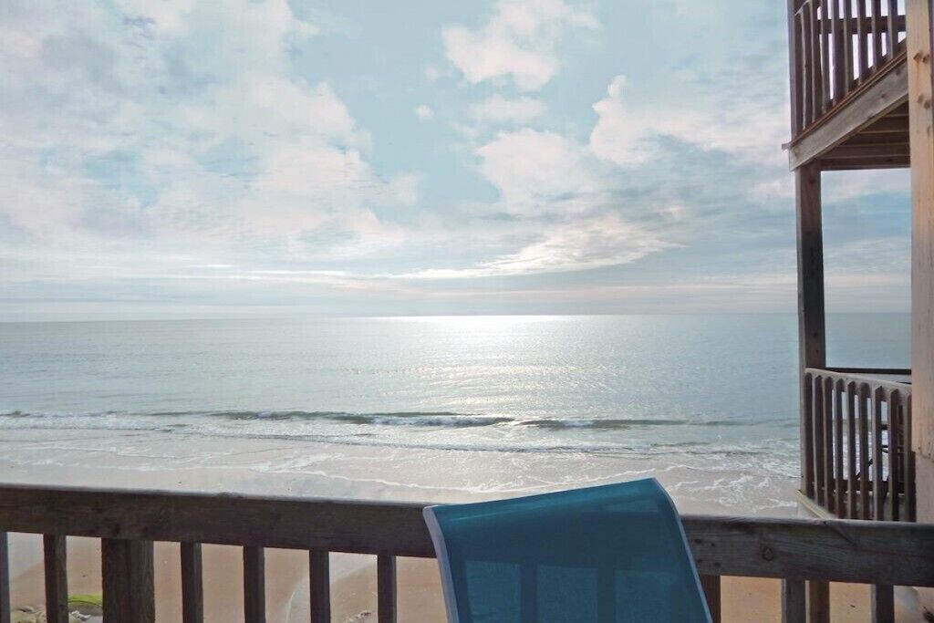 A beach view from a wooden deck with a chair.
