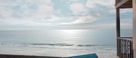A beach view from a wooden deck with a chair.