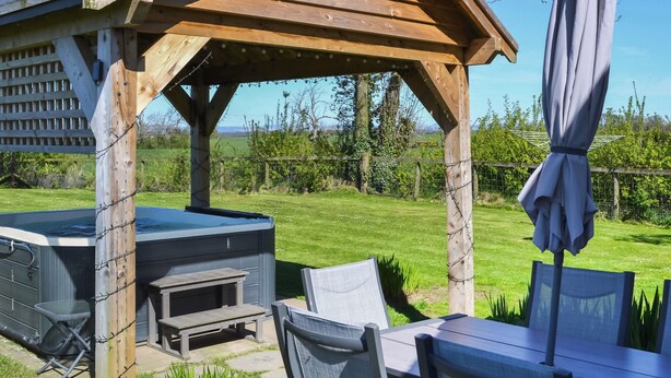 A wooden gazebo with a hot tub, outdoor seating, and a table with an umbrella. - 3 bedroom accommodation in Carlisle (Carlisle)