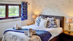 A bedroom with a bed, two bedside lamps, a window with a view, and a patterned wall. - 3 bedroom accommodation in Carlisle (Carlisle)