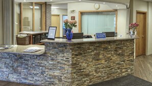 A reception desk with a stone facade, a clock on the wall, and a vase with flowers.