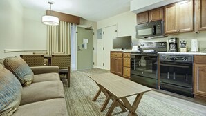 A compact living space with a sofa, a dining table, a kitchen area including a microwave, stove, and cabinets.