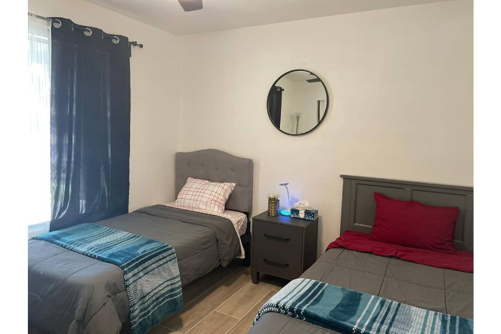 A bedroom with two beds, a nightstand, a mirror, and a window with curtains.