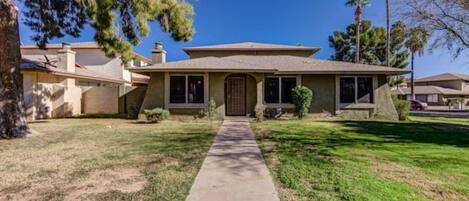 A single-story house with a front yard, a driveway, and a clear sky.