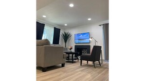 Een moderne woonkamer met een bank, fauteuil en een flatscreen televisie aan de muur.