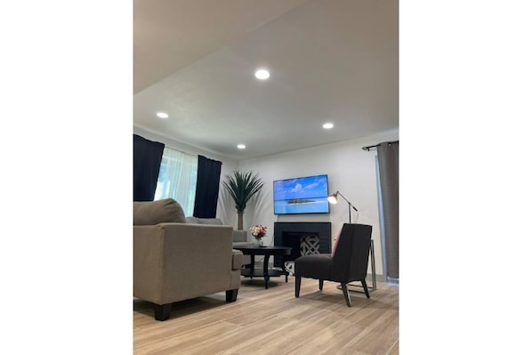 Ein modernes Wohnzimmer mit einer Couch, einem Sessel und einem wandmontierten Flachbildfernseher.
