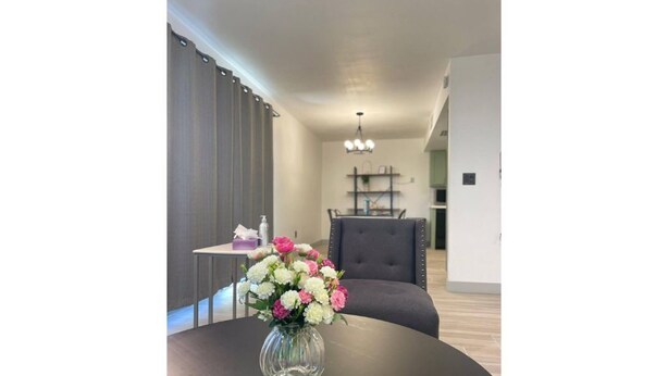 Een moderne woonkamer met een ronde tafel, een bloemenvaas, een afstandsbediening en een grijze fauteuil.