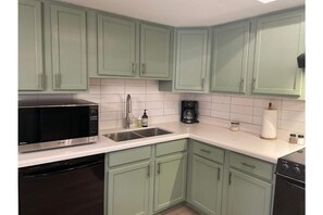 A kitchen with light green cabinets, a stainless steel sink, a black microwave, and a black dishwasher.