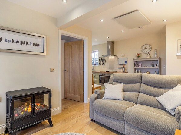 A living room with a sofa, a fireplace, and a kitchen in the background.