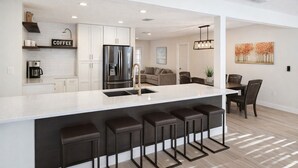 Una cocina moderna con una isla central, taburetes de bar, un refrigerador y una estación de café.