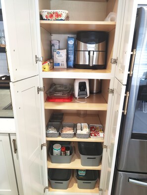 Una cocina con alacenas abiertas, que contiene varios electrodomésticos y recipientes de almacenamiento.