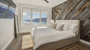 Un dormitorio con una cama grande, un ventilador de techo, un ventanal con vista a la montaña y un panel de pared de madera.
