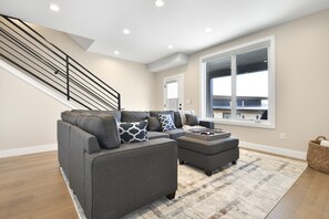 A modern living room with a gray sectional sofa, ottoman, and a large window providing a view of the outside.
