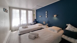 A hotel room with two beds, a blue accent wall, and a window with sheer curtains. - Beach la gravière Villa F4 between Lake and Sea with reversible air conditioning in Hossegor (SOORTS HOSSEGOR)