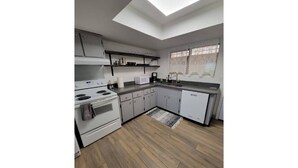 A modern kitchen with a skylight, white cabinets, and a wooden floor. - Msg for 5%off_2Bed1Bath KingQueenBeds NorthPHX (Phoenix)