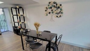 A modern dining area with a wooden floor, a black dining table, and chairs. There is a decorative wall art of a tree and a black shelving unit with a vase on top. - Msg for 5%off_2Bed1Bath KingQueenBeds NorthPHX (Phoenix)