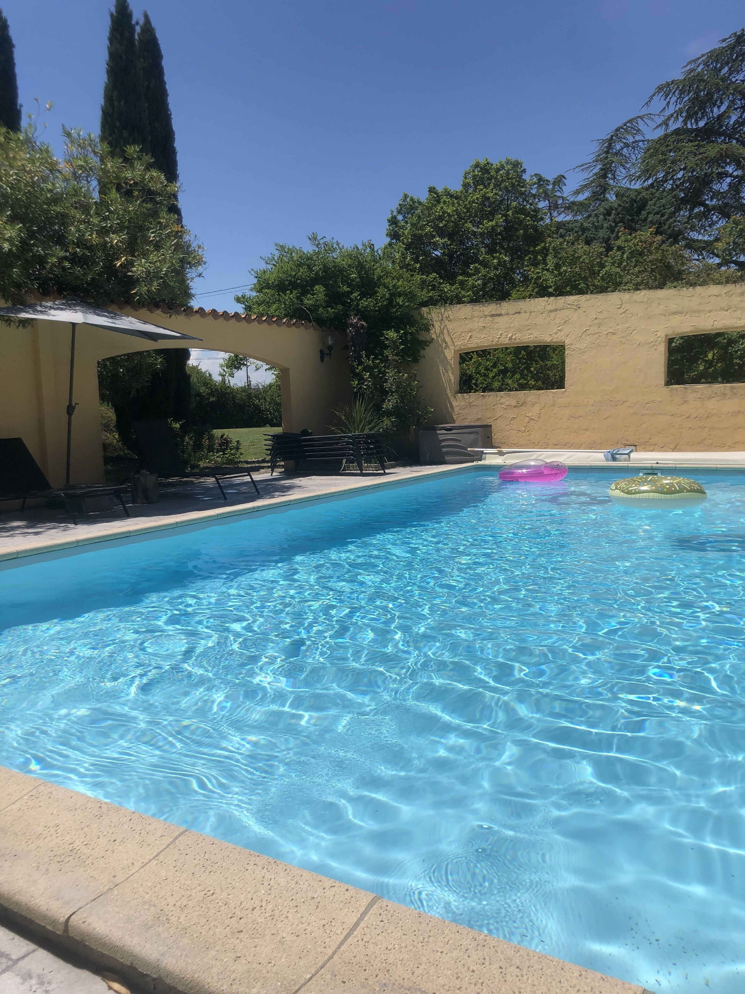 Une piscine aux eaux cristallines, bordée de carreaux, entourée d’un espace de repos couvert comprenant des bancs et une pergola.