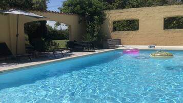 Une piscine aux eaux cristallines, bordée de carreaux, entourée d’un espace de repos couvert comprenant des bancs et une pergola.