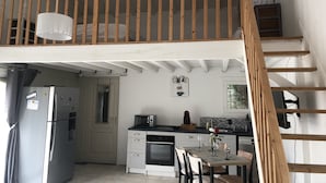 Una cocina con comedor, microondas, refrigerador y una escalera de madera.