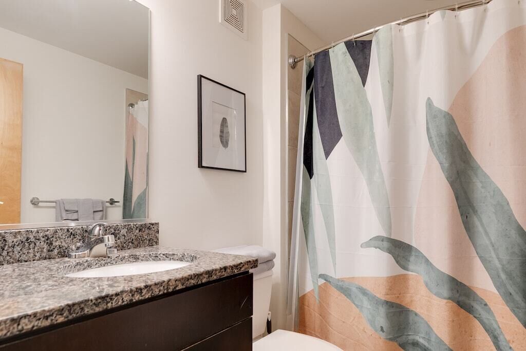 A bathroom with a granite countertop sink, a framed picture on the wall, and a shower curtain with abstract leaf patterns.