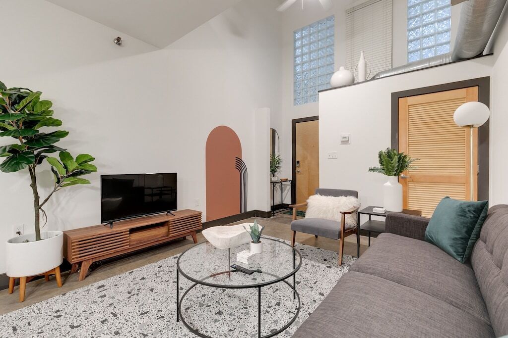 Ein modernes Wohnzimmer mit einem Flachbildfernseher, einem Glastisch, einem grauen Sofa und einer Topfpflanze.