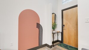 A hallway with a large archway, a wooden door, a small table with a plant, and a mirror on the wall. - Atrium 105 - Lovely 1-Bedroom Loft (Richmond)