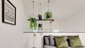 A modern bedroom with a bed, pillows, a bedside table, a lamp, and hanging plants. - Atrium 105 - Lovely 1-Bedroom Loft (Richmond)