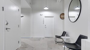 A hallway with white walls, a round mirror, and two black chairs with a small white table. - Downtown Living in Richmond's Amazing Shockoe Bottom (Richmond)