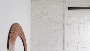 A minimalist bedroom with a green quilted bedspread, a white wall with a textured white brick pattern, and a wooden decorative piece with tassels. - Downtown Living in Richmond's Amazing Shockoe Bottom (Richmond)