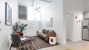 A modern living room with a sofa, armchair, and coffee table, a dining area with a table and chairs, and a kitchen with a refrigerator. - Downtown Living in Richmond's Amazing Shockoe Bottom (Richmond)