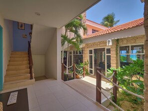 A spacious indoor area with a staircase leading to a balcony, a stone wall, and a view of the outside. - Casa del Navegante  -  Yucatan Home Rentals (Progreso)