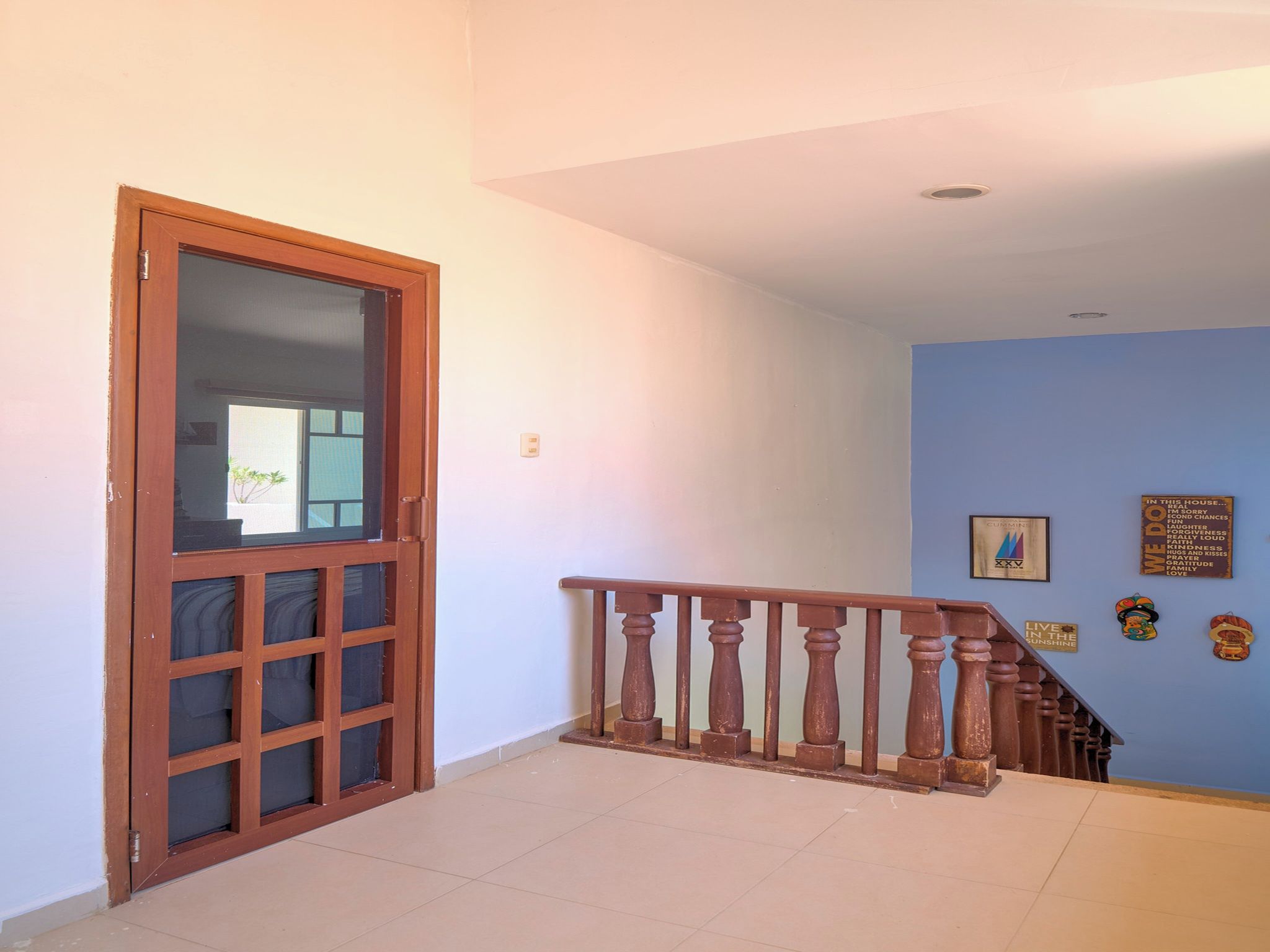 A hallway with a wooden door, a staircase with a wooden railing, and a blue wall with decorative items.
