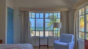 Une chambre à coucher comprenant un lit, une chaise, une petite table et une fenêtre donnant sur la plage et l’océan.