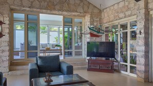 Un salon spacieux avec un mur en pierre, une grande porte-fenêtre coulissante donnant sur un balcon, un téléviseur et une table basse.